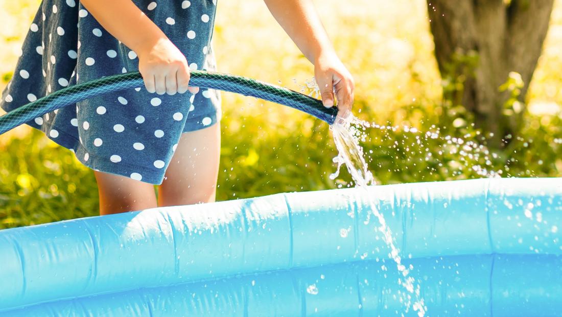 enfant tenant un tuyau d'arrosage pour remplir sa piscine