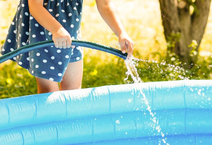 enfant tenant un tuyau d'arrosage pour remplir sa piscine